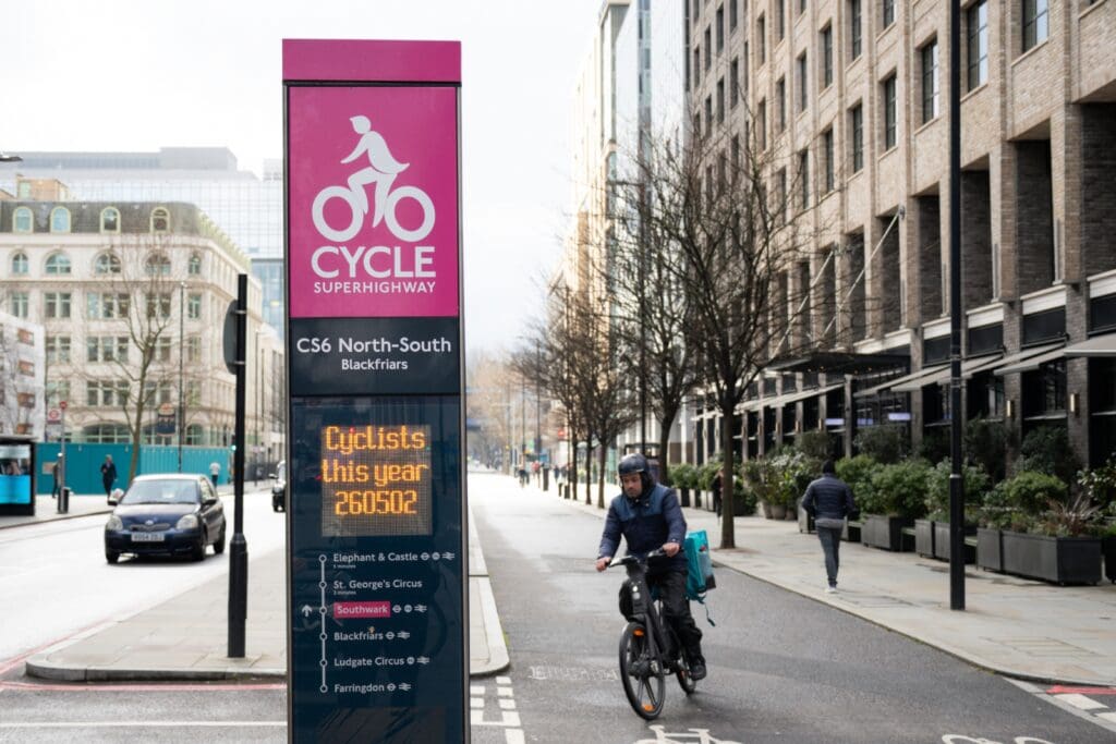 A cyclist in London cycling on a cycle path and a digital display sign show the number of cyclist who cycled on it