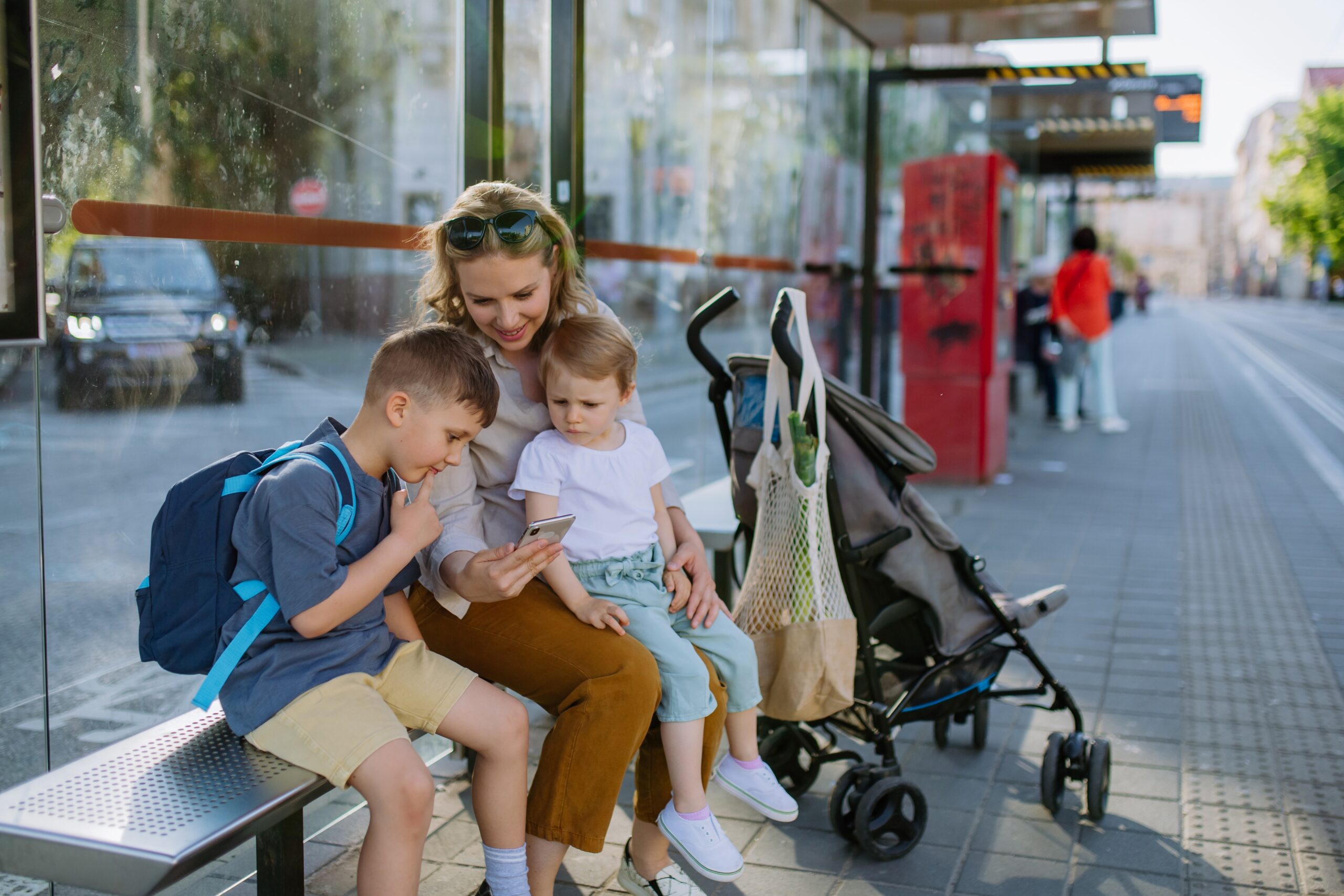 Women with two young children waiting at bus stop. Also a pushchair with groceries